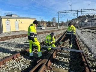 Tre fagfolk kontrollerer sporveksel med måleutstyr ute i sporet
